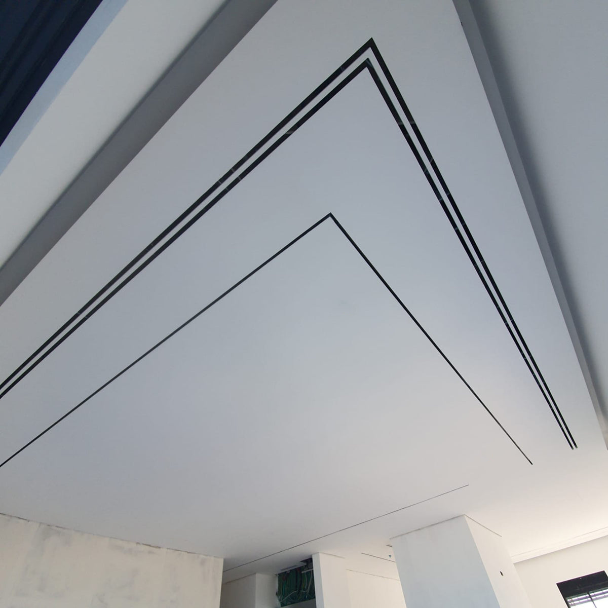 White ceiling with Cryptic Air 2-slot mud-in linear diffuser, black grooves form geometric pattern, viewed below.